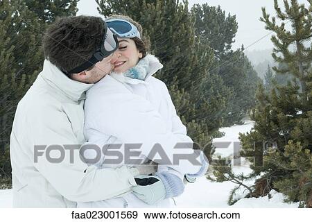 Stock Photo - Young couple dressed in ski clothes kissing. Fotosearch
