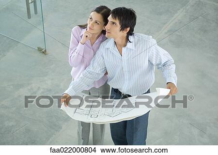 Young couple holding blueprints, looking up, high angle view View Large Photo Image Picture - Young couple holding blueprints, looking up, high angle view. Fotosearch