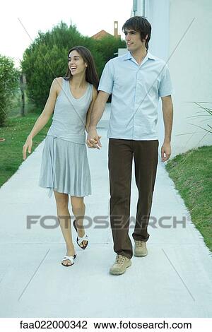 Young couple holding hands as they walk down sidewalk, looking out of frame View Large Photo Image Stock Image - Young couple holding hands as they walk down sidewalk, looking out of frame. Fotosearch
