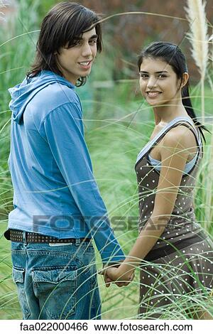 Stock Photograph - Young couple holding hands, looking over shoulders at camera. Fotosearch