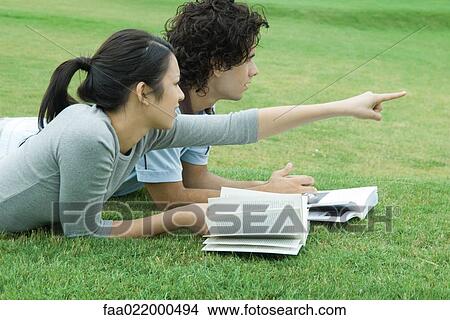Young couple lying on grass with books, woman pointing, both looking out of frame View Large Photo Image Picture - Young couple lying on grass with books, woman pointing, both looking out of frame. Fotosearch