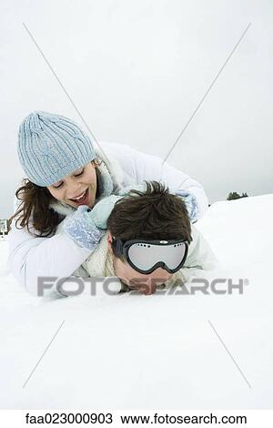 Stock Image - Young couple lying on the ground in snow, one on top of the other, smiling. Fotosearch