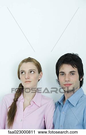 Stock Image - Young couple, man looking at camera while woman looks away, portrait. Fotosearch