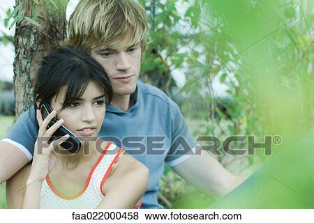 Stock Photo - Young couple next to tree, woman using cell phone. Fotosearch