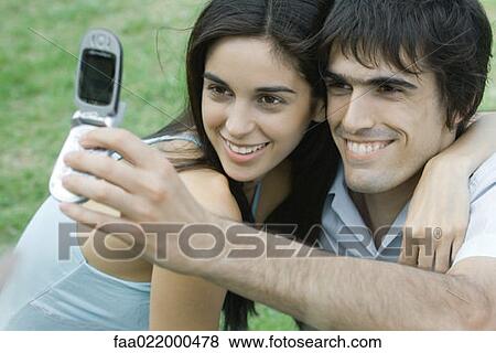 Stock Photo - Young couple posing while man holds up cell phone to take photo. Fotosearch
