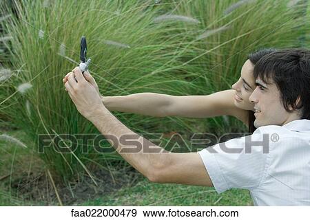 Young couple posing while man holds up cell phone to take photo View Large Photo Image Stock Photo - Young couple posing while man holds up cell phone to take photo. Fotosearch