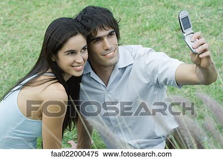 Young couple posing while man holds up cell phone to take photo View Large Photo Image Stock Photography - Young couple posing while man holds up cell phone to take photo. Fotosearch