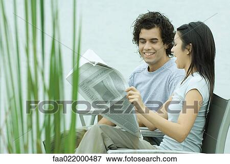 Young couple reading newspaper together by edge of lake View Large Photo Image Stock Photo - Young couple reading newspaper together by edge of lake. Fotosearch