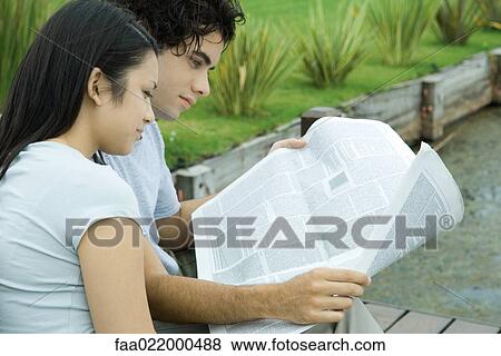 Stock Photo - Young couple reading newspaper together outdoors. Fotosearch