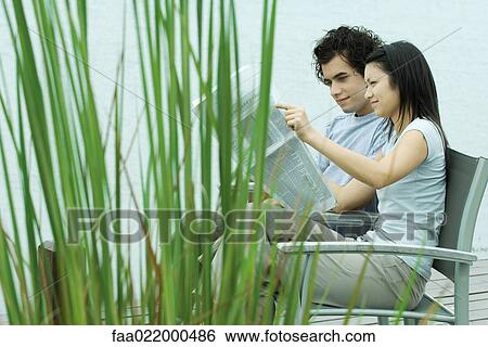 Young couple reading newspaper together by edge of lake View Large Photo Image Stock Photograph - Young couple reading newspaper together by edge of lake. Fotosearch