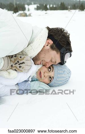 Stock Photo - Young couple reclining in snow together, smiling, one on top of the other. Fotosearch