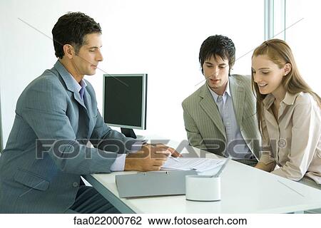 Young couple sitting across desk from businessman, businessman pointing to document View Large Photo Image Stock Image - Young couple sitting across desk from businessman, businessman pointing to document. Fotosearch