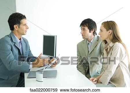 Young couple sitting across desk from businessman, businessman holding document and speaking View Large Photo Image Stock Photo - Young couple sitting across desk from businessman, businessman holding document and speaking. Fotosearch
