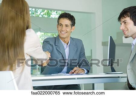 Young couple sitting across desk from businessman, woman shaking hands with businessman View Large Photo Image Stock Photography - Young couple sitting across desk from businessman, woman shaking hands with businessman. Fotosearch