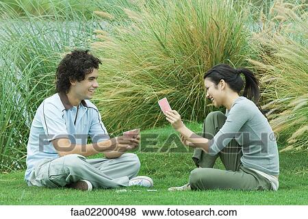 Young couple sitting on grass playing cards View Large Photo Image Stock Photo - Young couple sitting on grass playing cards. Fotosearch