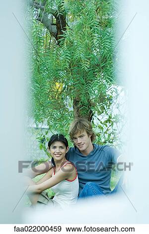 Young couple sitting under tree, portrait View Large Photo Image Stock Photo - Young couple sitting under tree, portrait. Fotosearch