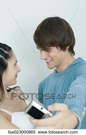 Stock Photography - Young couple smiling at each other, man taking photo with digital camera. Fotosearch