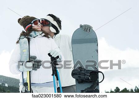 Young couple standing outside with skis and snowboard, man kissing girlfriend's cheek View Large Photo Image Stock Image - Young couple standing outside with skis and snowboard, man kissing girlfriend's cheek. Fotosearch