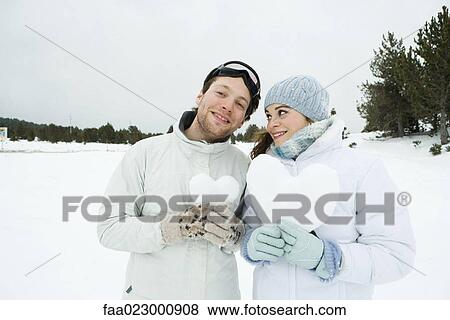 Young couple standing side by side, holding hearts made of snow, portrait View Large Photo Image Stock Photo - Young couple standing side by side, holding hearts made of snow, portrait. Fotosearch