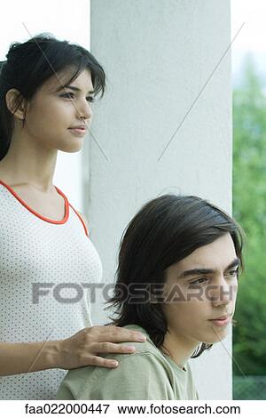 Stock Photo - Young couple, woman standing with hand on boyfriend's shoulder. Fotosearch