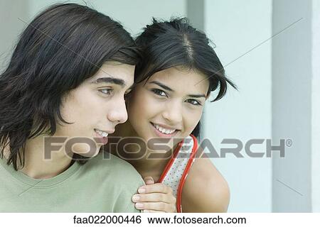 Stock Photograph - Young couple, young woman looking over boyfriend's shoulder at camera. Fotosearch
