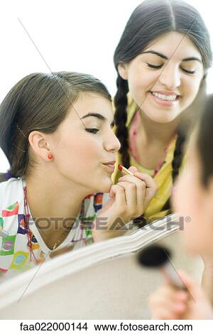 Young female friends looking at mirror, putting on make-up View Large Photo Image Picture - Young female friends looking at mirror, putting on make-up. Fotosearch