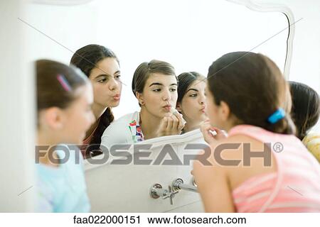 Young female friends looking at mirror, putting on make-up View Large Photo Image Stock Image - Young female friends looking at mirror, putting on make-up. Fotosearch