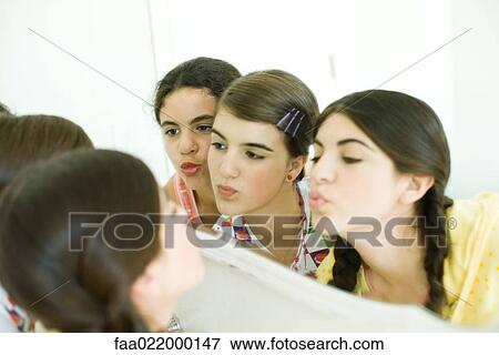 Stock Photo - Young female friends looking at mirror, putting on make-up. Fotosearch