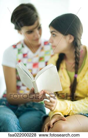 Young female friends reading book together, looking at each other View Large Photo Image Stock Photo - Young female friends reading book together, looking at each other. Fotosearch