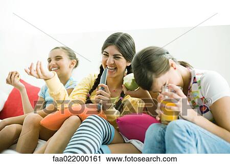 Stock Image - Young female friends sitting side by side, laughing. Fotosearch