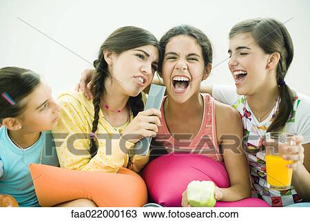 Young female friends sitting together, one singing into remote control as others laugh View Large Photo Image Stock Image - Young female friends sitting together, one singing into remote control as others laugh. Fotosearch