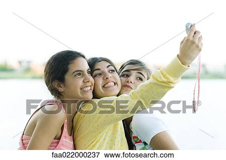 Young female friends taking photo of selves with cell phone View Large Photo Image Stock Photo - Young female friends taking photo of selves with cell phone. Fotosearch