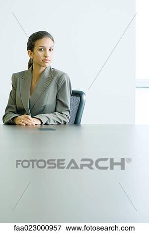 Young female in business attire sitting at table, looking at camera, portrait View Large Photo Image Stock Photo - Young female in business attire sitting at table, looking at camera, portrait. Fotosearch