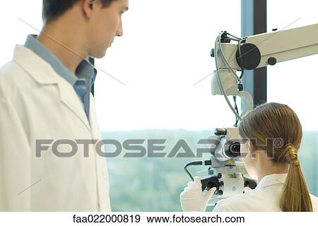 Young female scientist looking through microscope, male colleague watching her View Large Photo Image Stock Photo - Young female scientist looking through microscope, male colleague watching her. Fotosearch