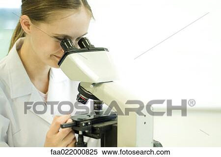 Stock Photography - Young female scientist looking through microscope. Fotosearch