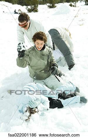 Stock Photograph - Young friends having snowball fight, one lying on ground, covering head with arms. Fotosearch