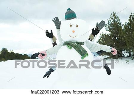 Stock Image - Young friends hiding behind snowman, arms out. Fotosearch