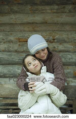 Young friends in winter clothes, one holding cards while the other gives her a hug View Large Photo Image Picture - Young friends in winter clothes, one holding cards while the other gives her a hug. Fotosearch