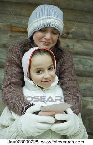 Young friends in winter clothes, one holding cards while the other gives her a hug View Large Photo Image Stock Photography - Young friends in winter clothes, one holding cards while the other gives her a hug. Fotosearch