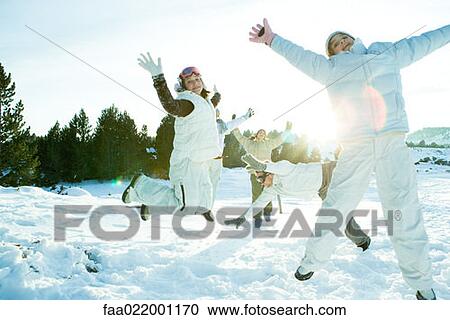 Stock Image - Young friends jumping in the air, dressed in winter clothing, full length. Fotosearch