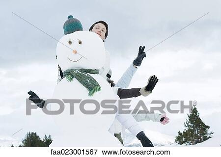 Stock Photo - Young friends sticking arms out from behind snowman. Fotosearch