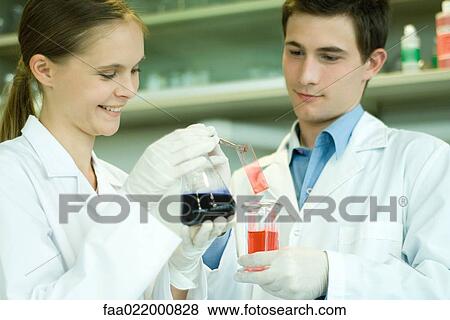 Young male and female scientists holding solutions in lab glassware View Large Photo Image Stock Photo - Young male and female scientists holding solutions in lab glassware. Fotosearch