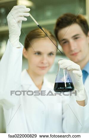 Young male and female scientists, woman holding up dropper and flask View Large Photo Image Stock Photo - Young male and female scientists, woman holding up dropper and flask. Fotosearch
