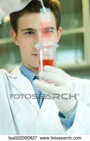 Stock Photo - Young male scientist dipping microscope slide into solution in test tube, holding up slide. Fotosearch