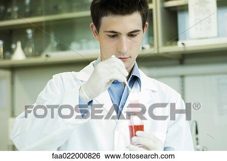 Stock Photograph - Young male scientist dipping microscope slide into solution in test tube. Fotosearch