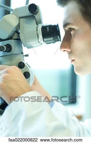 Stock Image - Young male scientist looking through microscope, close-up. Fotosearch