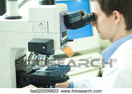 Stock Image - Young male scientist looking through microscope. Fotosearch
