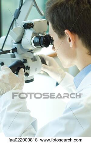 Stock Photo - Young male scientist looking through microscope. Fotosearch