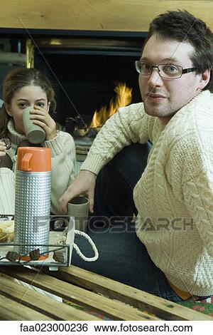 Young man and teen girl drinking hot drinks by fire place View Large Photo Image Stock Photograph - Young man and teen girl drinking hot drinks by fire place. Fotosearch