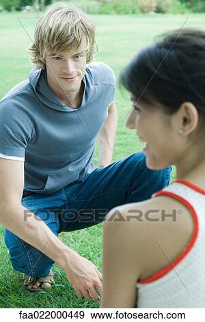 Stock Photo - Young man and woman, man crouching on lawn looking at woman. Fotosearch